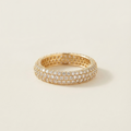 A gold eternity ring paved with small clear stones, photographed on a clean, light beige background.