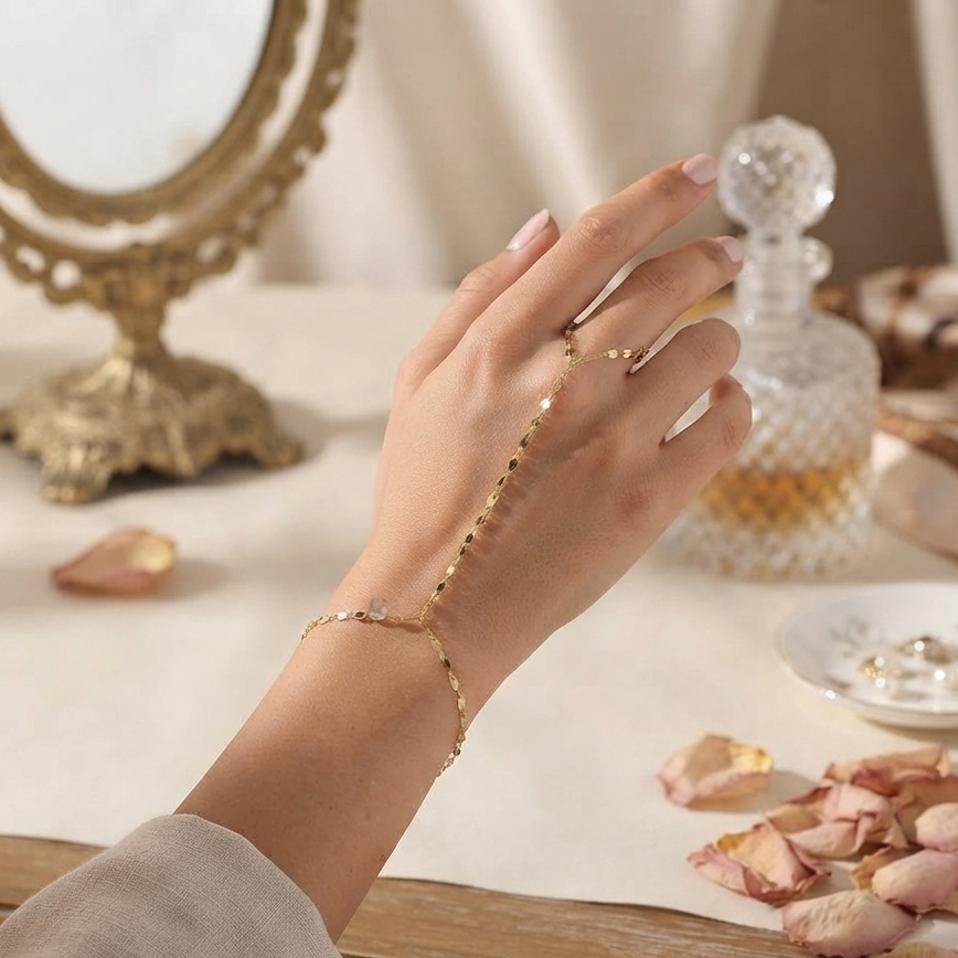 A delicate gold chain bracelet and matching ring worn on a woman's hand, styled with dried rose petals and a vintage gold mirror on a table.