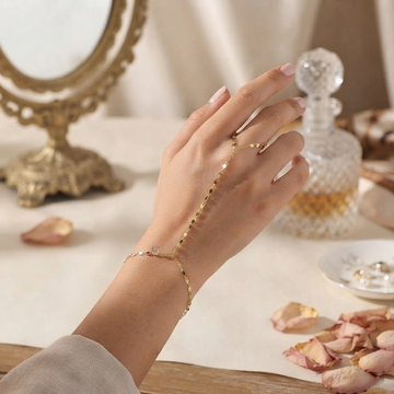 A delicate gold chain bracelet and matching ring worn on a woman's hand, styled with dried rose petals and a vintage gold mirror on a table.
