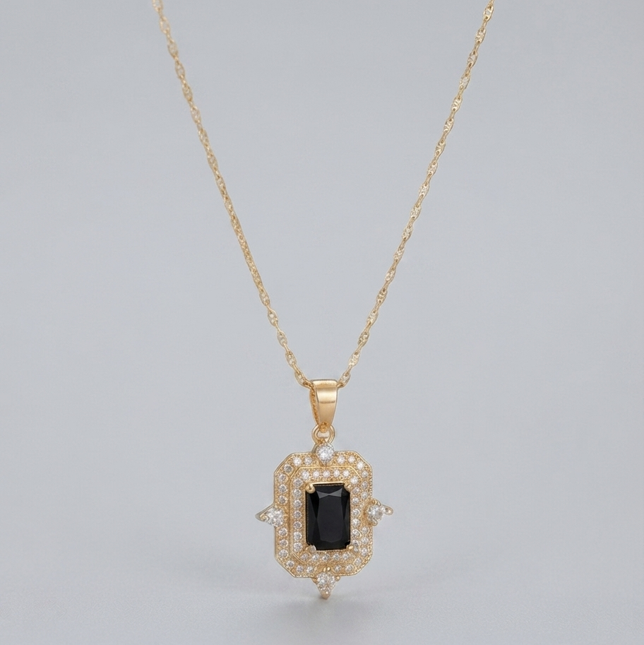 A gold pendant necklace featuring a rectangular black gemstone surrounded by a halo of small clear stones, suspended from a delicate gold chain against a light gray background.