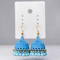 A pair of light blue jhumka earrings with gold-tone hooks and bead accents, displayed on a white branded card against a light gray background.