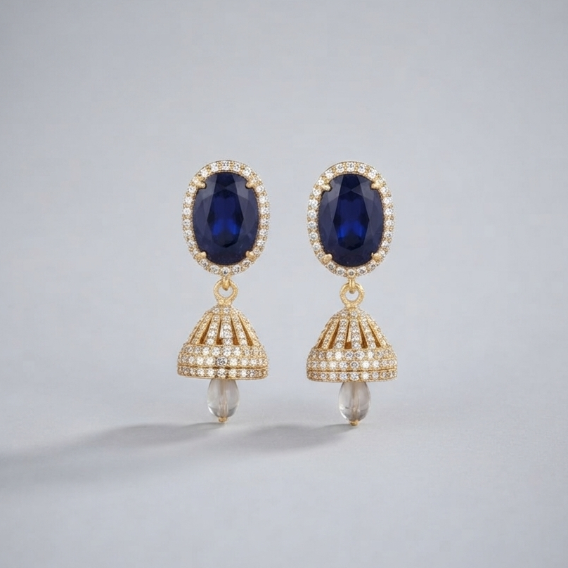 A pair of gold drop earrings featuring oval deep blue gemstones surrounded by small clear stones, with dangling bell-shaped gold sections set with clear stones and small pearl-like drops at the bottom, shown on a light gray background.
