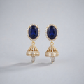 A pair of gold drop earrings featuring oval deep blue gemstones surrounded by small clear stones, with dangling bell-shaped gold sections set with clear stones and small pearl-like drops at the bottom, shown on a light gray background.