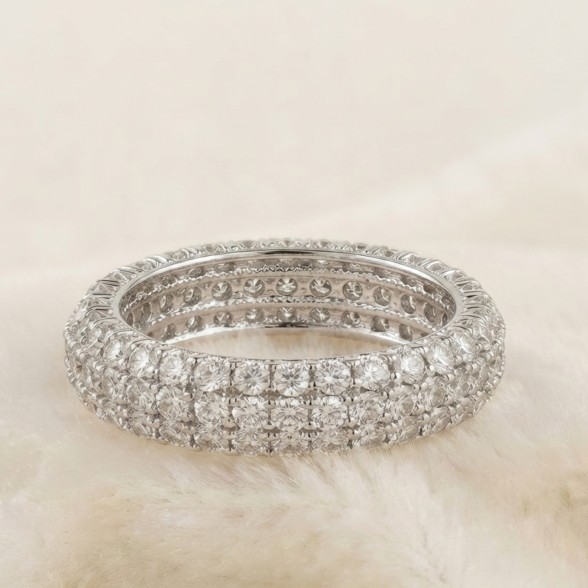 A silver-toned diamond eternity ring with three rows of pavé-set round diamonds, photographed on a soft cream faux fur surface.