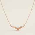 A delicate rose gold chain necklace featuring a small central pendant with a stylized leaf or vine motif, displayed against a clean, solid off-white background.