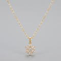 A delicate yellow gold chain necklace with a small snowflake-shaped pendant paved with clear stones, displayed against a neutral gray background.