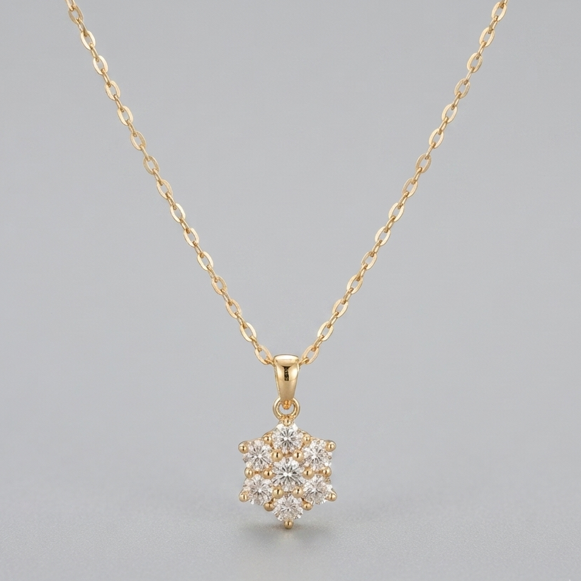 A delicate yellow gold chain necklace with a small snowflake-shaped pendant paved with clear stones, displayed against a neutral gray background.