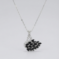 A silver-toned necklace featuring a pendant shaped like a swan with a black leafy branch for its body, set against a plain light gray background.
