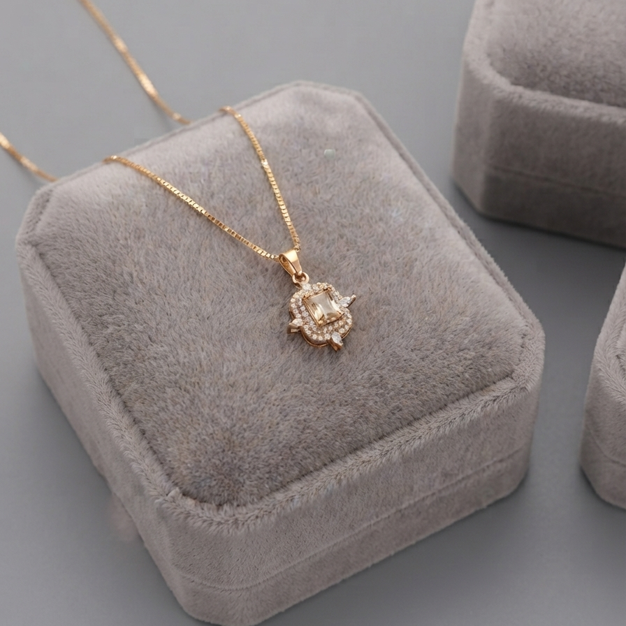 A gold pendant necklace with a black rectangular center stone and surrounding clear stones, displayed on a soft beige fabric surface.