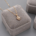 A gold chain necklace with a small floral cluster pendant displayed on a gray velvet jewelry box.