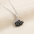 A silver-toned necklace with a swan pendant featuring black teardrop-shaped stones and clear rhinestone accents, displayed on a soft beige fabric background.