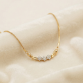 A delicate gold chain necklace with a short section of clear pavé gemstones in the center, displayed on a soft beige fabric background.