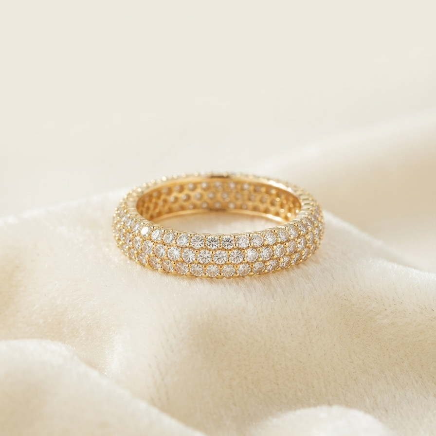 A gold eternity ring paved with small clear stones, resting on a soft beige fabric surface.