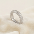 A silver pavé ring with a textured inner band, resting on a soft, cream-colored fabric background.