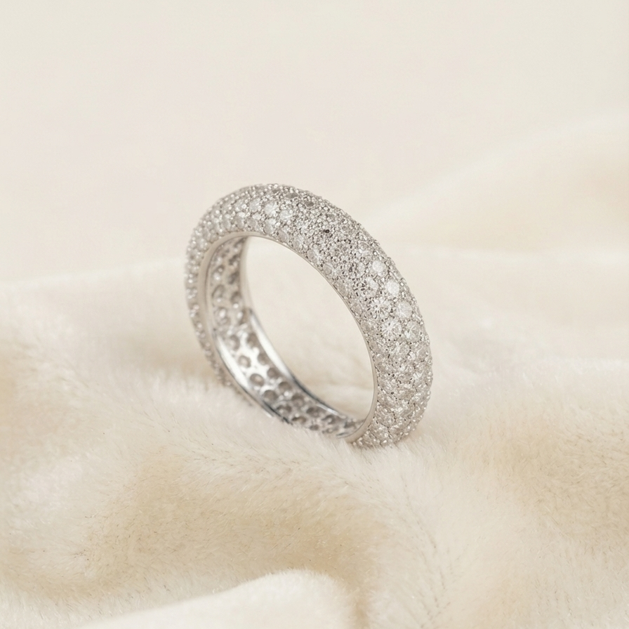 A silver pavé ring with a textured inner band, resting on a soft, cream-colored fabric background.