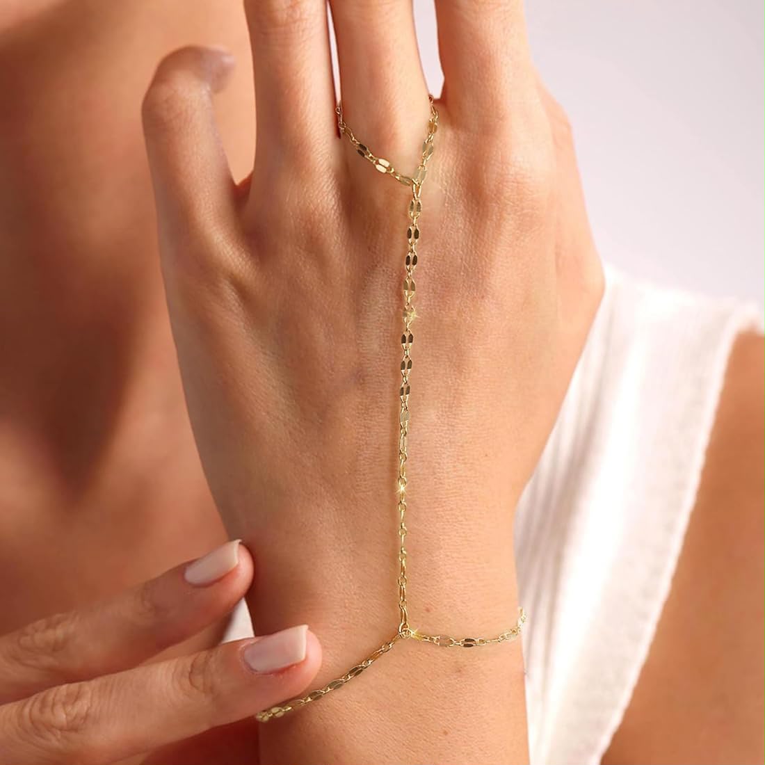 A delicate gold chain bracelet and matching ring worn on a woman's hand, styled with dried rose petals and a vintage gold mirror on a table.