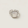 A silver-toned double-band ring with a square-shaped, milky white mother-of-pearl center stone, photographed on a clean, light beige background.