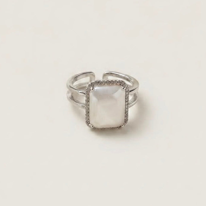 A silver-toned double-band ring with a square-shaped, milky white mother-of-pearl center stone, photographed on a clean, light beige background.